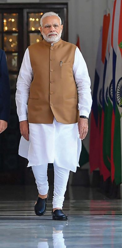 Indian Prime Minister Narendra Modi, wearing a traditional beige Nehru jacket over a white kurta-pyjama, illustrates the classic bandhgala silhouette and the modern political and cultural significance of the Nehru jacket in Indian menswear.