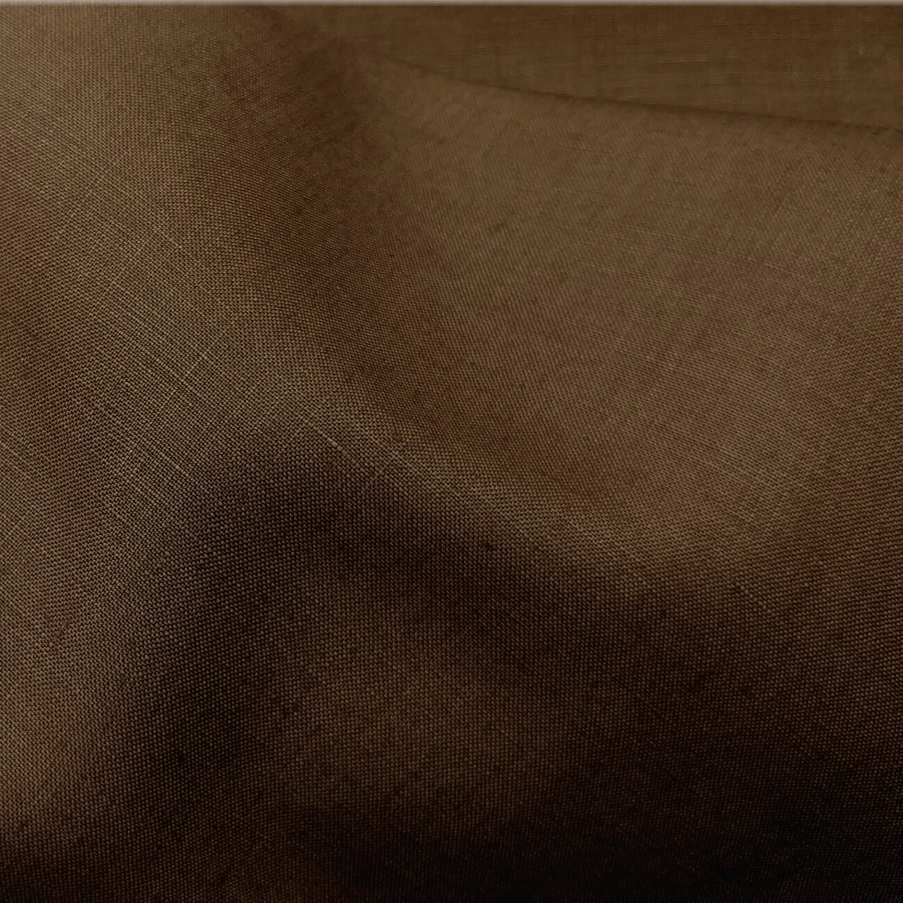 Dark tan Baird McNutt mercerized linen suiting fabric, fully shrunk, close-up showing smooth refined weave, warm sienna tone, and soft drape, premium breathable linen for luxury suits, tailored jackets, and sophisticated warm-weather menswear.